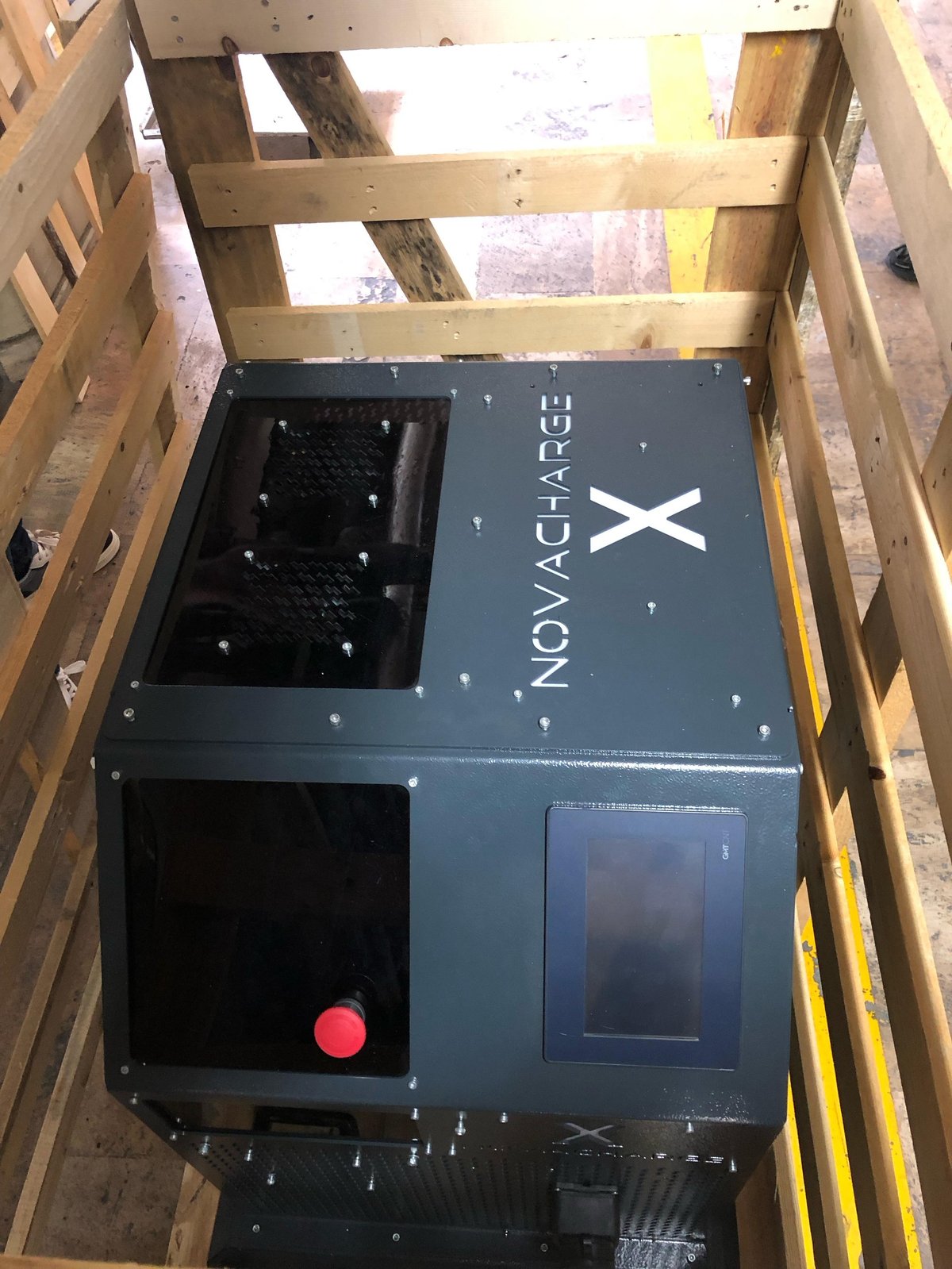 Novachrge X electric vehicle charging station in wooden crate with red indicator light visible