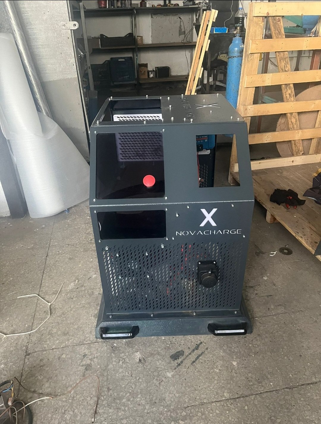 Novacharge electric vehicle charging station in garage with red charging indicator and industrial shelving in background
